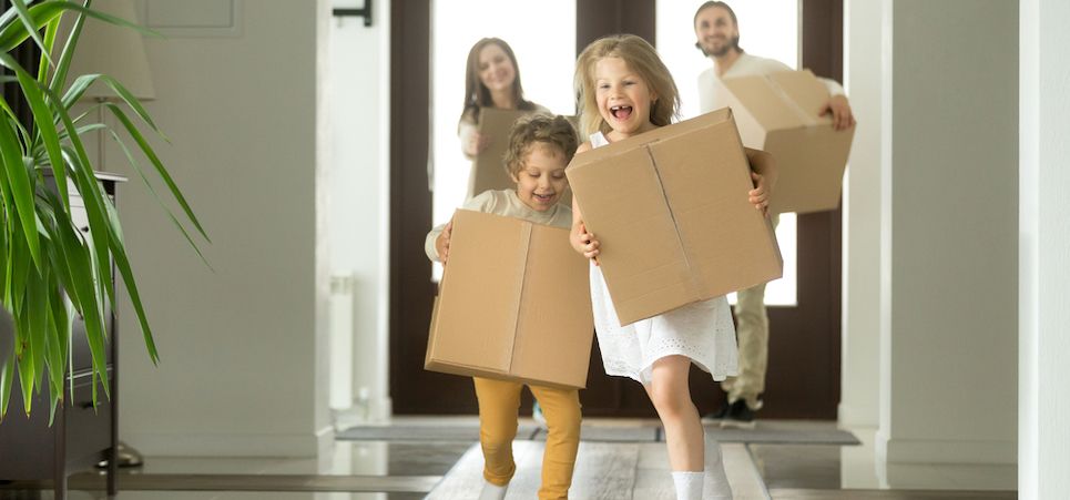 Young family with two children running into home holding boxes