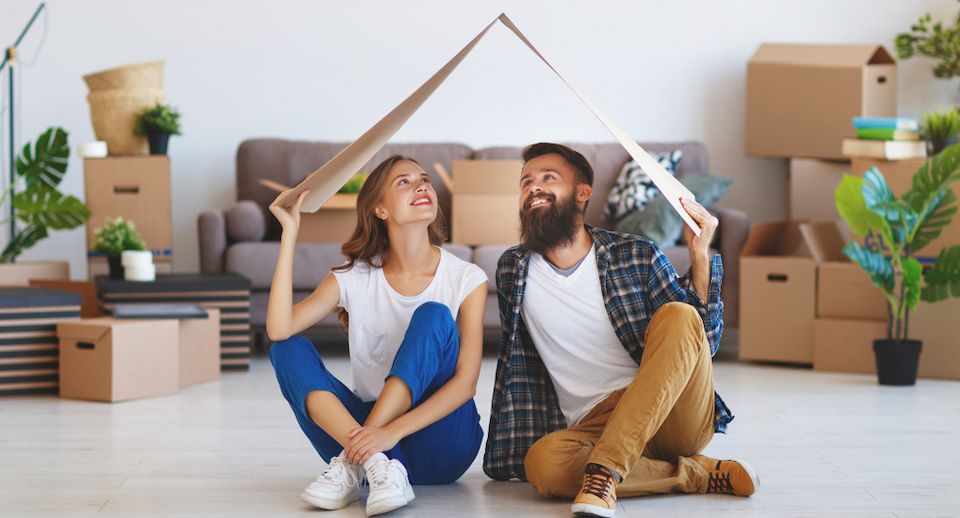Young couple surrounded by moving boxes holding box above head
