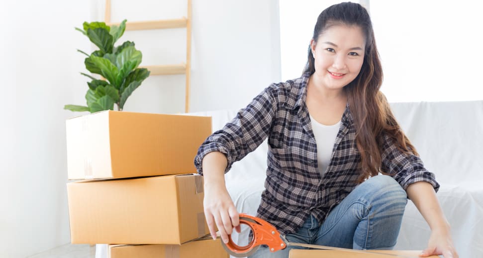 Young asian woman taping box next to other moving boxes