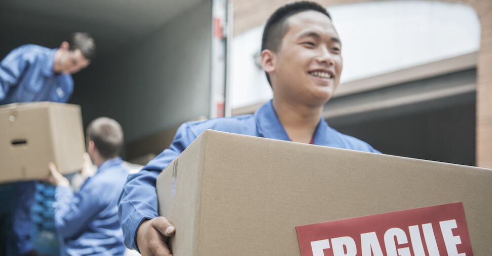 Smiling Asian working carrying fragile box in front of moving truck