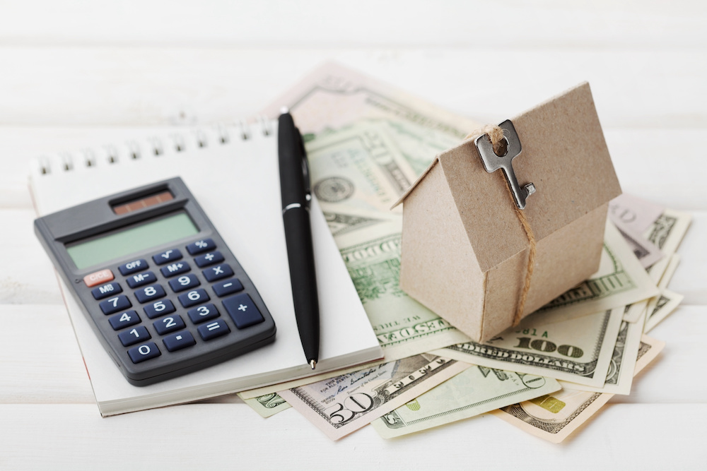 Model of cardboard house with key, calculator, notebook, pen and cash dollars. House building, loan, real estate. Cost of public utilities, insurance, rent or buying a new home concept