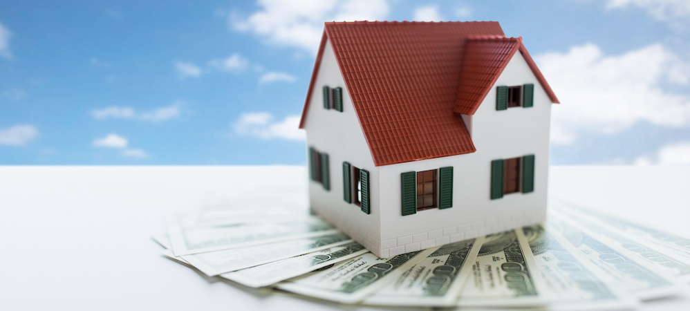 mortgage, real estate and property concept - close up of home or house model and money over blue sky and clouds background