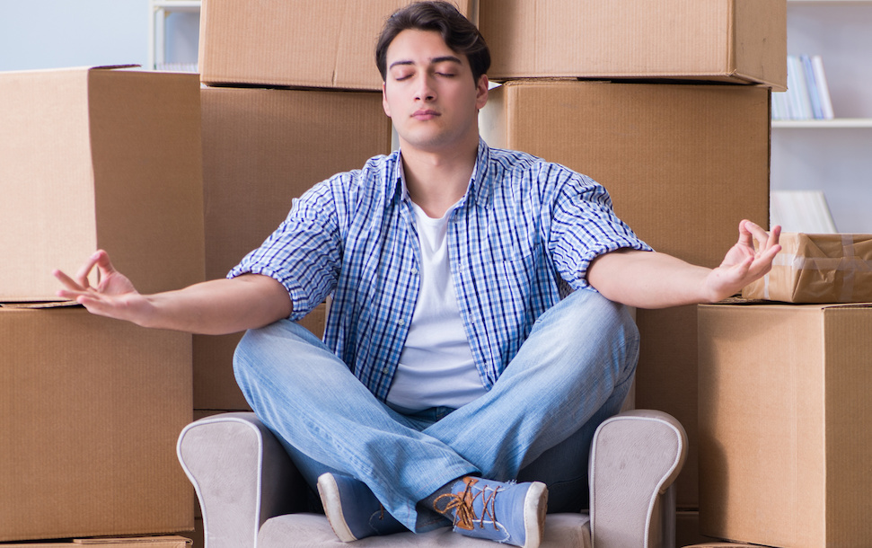 Young man meditating in front of moving boxes