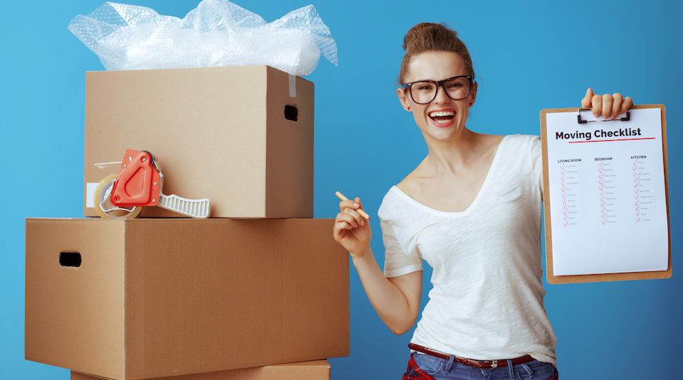 smiling woman holding pen and checklist next to moving boxes